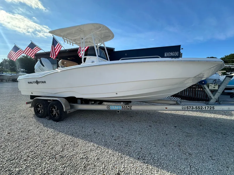 Slide: The Image of 2025 NauticStar 231 Hybrid boat on trailer with American flags in background. - 3