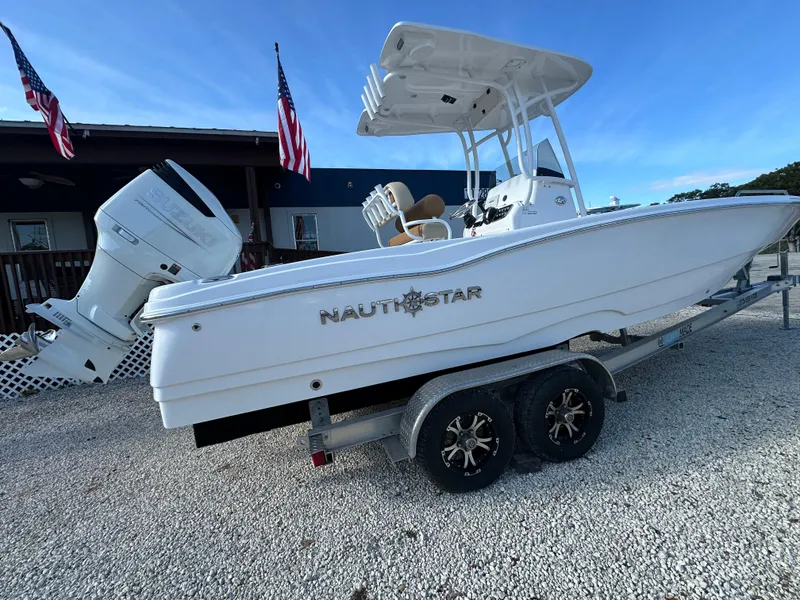 Slide: The Image of 2025 NauticStar 231 Hybrid boat on trailer, displayed outdoors with flags. - 4