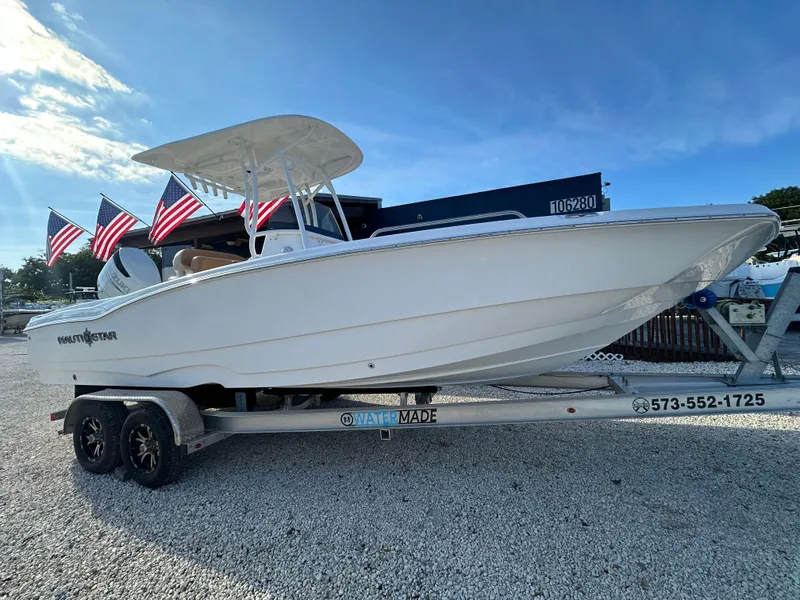 Slide: The Image of 2025 NauticStar 231 Hybrid boat on trailer with American flags, under clear blue sky. - 5