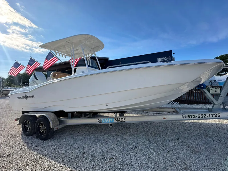 Slide: The Image of 2025 NauticStar 231 Hybrid boat on trailer with American flags in background. - 6