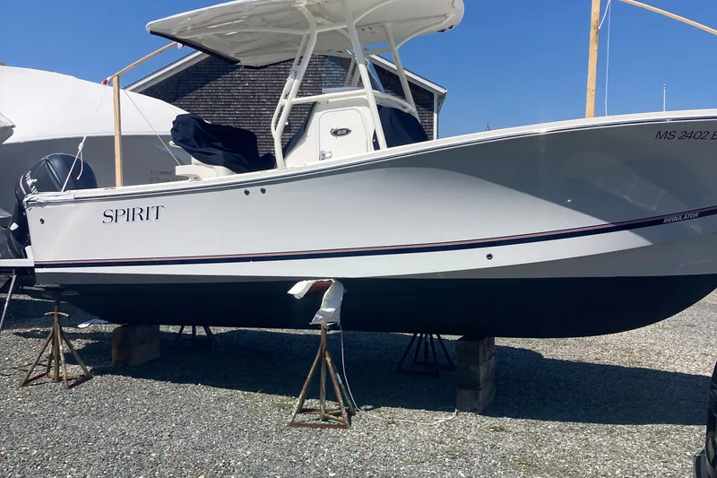 Slide: The Image of 2017 Regulator 23 Forward Seating boat on stands, labeled "Spirit," in a gravel yard. - 2
