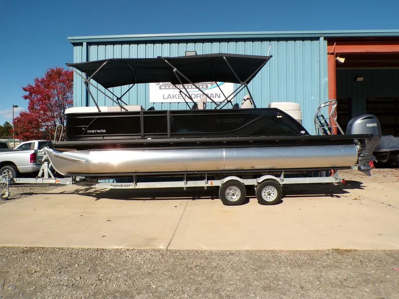 The Image of 2025 Godfrey Sweetwater 2286 QS pontoon boat on trailer, parked outside a blue building. - 1