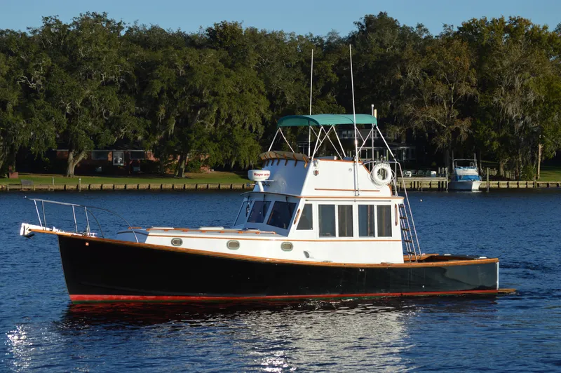 The Image of 1990 Stanley Downeast Lobster Boat cruising on a serene lake with lush green trees. - 0