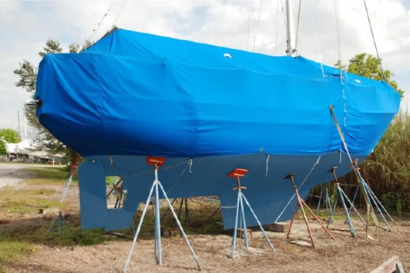 Slide: The Image of 1990 Pacific Seacraft 34 sailboat covered in blue tarp on stands. - 7
