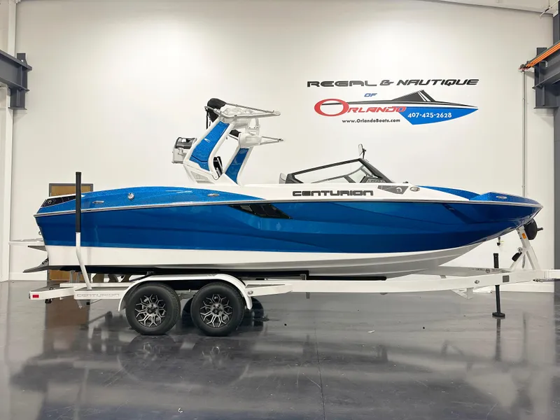 The Image of 2025 Centurion Fe23 boat in showroom, blue and white design on trailer. - 1