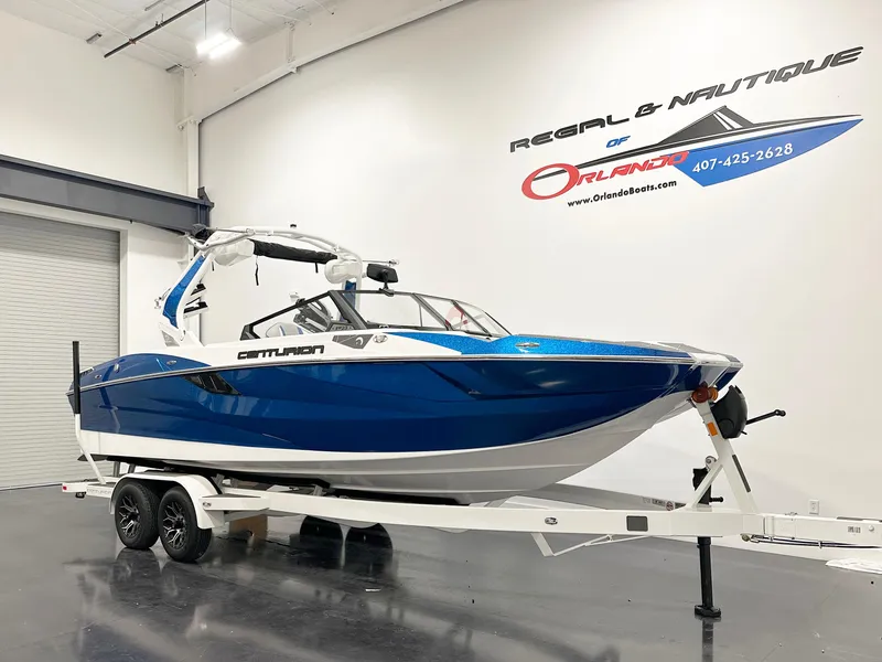Slide: The Image of 2025 Centurion Fe23 boat in showroom, blue and white design on trailer. - 2