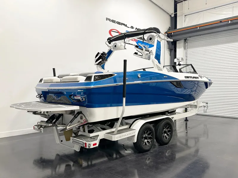 Slide: The Image of 2025 Centurion Fe23 boat on trailer in showroom, blue and white design. - 3