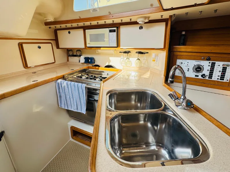 Slide: The Image of 1998 Catalina 320 yacht kitchen with dual sinks, stove, and wooden cabinetry. - 19
