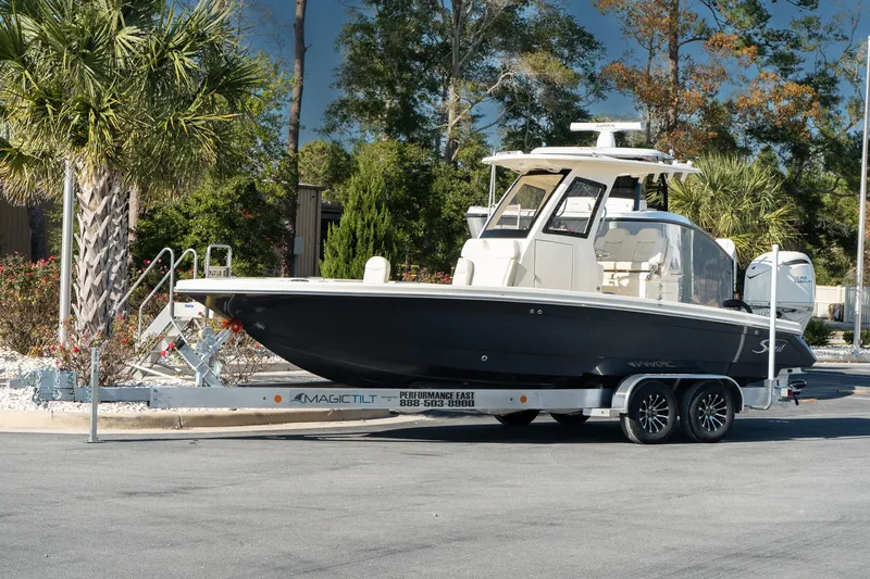 Slide: The Image of 2025 Scout 261 XSS boat on trailer, parked outdoors near palm trees. - 2