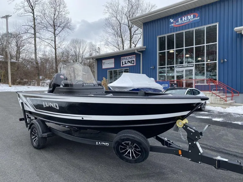 Slide: The Image of 2025 Lund 1775 Impact XS SS boat on trailer outside dealership in winter setting. - 17