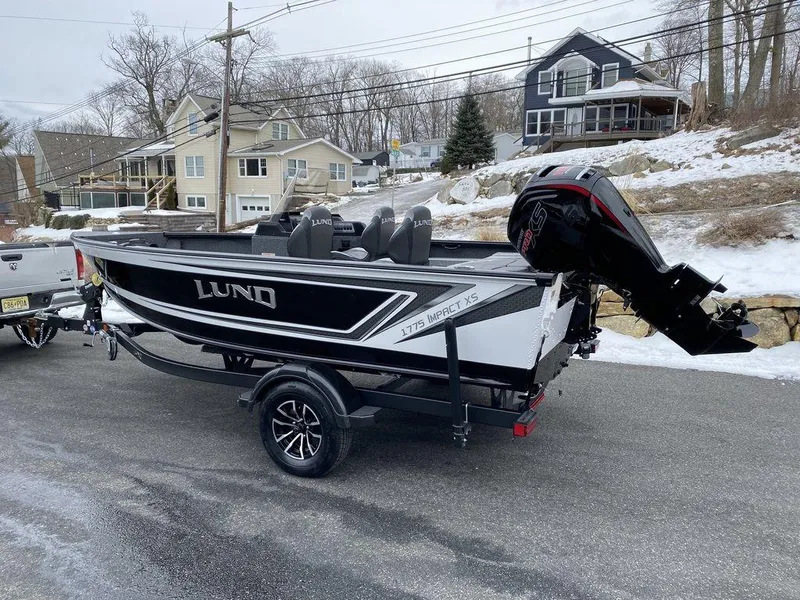 Slide: The Image of 2025 Lund 1775 Impact XS SS boat on trailer, parked on snowy street. - 3