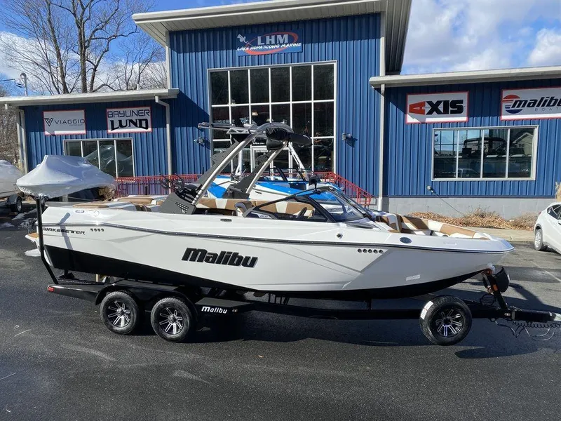 The Image of 2025 Malibu 23 LSV boat on trailer outside dealership, blue building in background. - 0