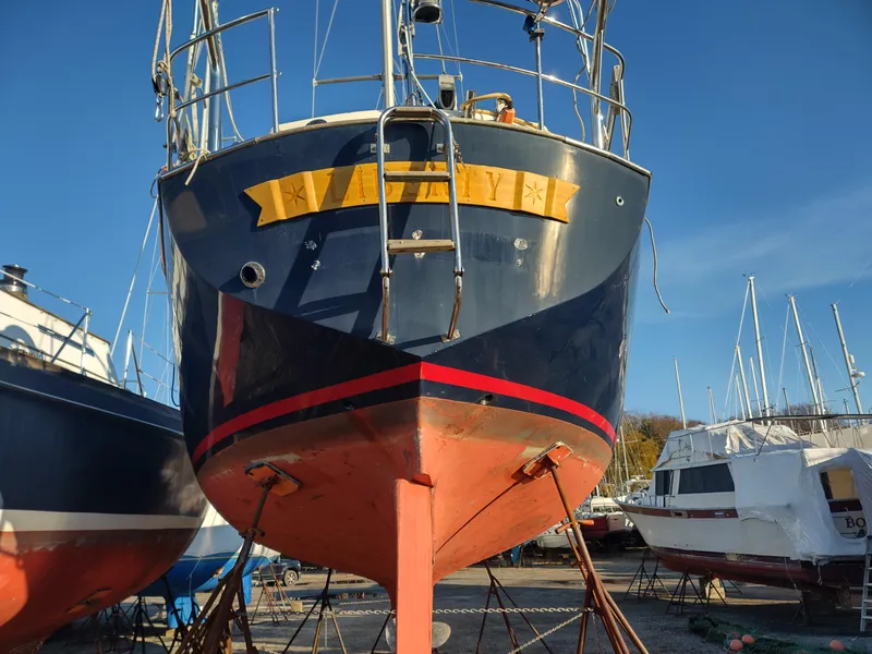 Slide: The Image of 1984 Belliure Sloop sailboat on dry dock, blue hull with red stripe, clear sky background. - 2