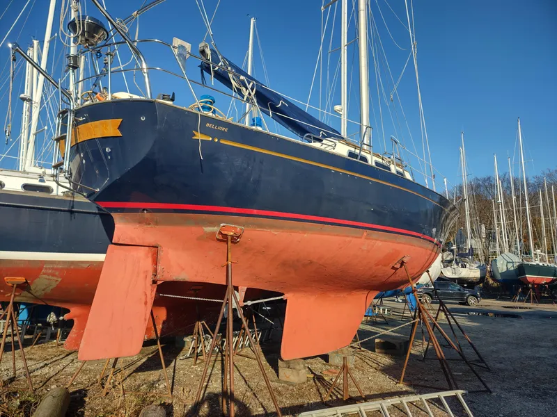 Slide: The Image of 1984 Belliure Sloop sailboat on dry dock, blue hull, red keel, clear sky background. - 4