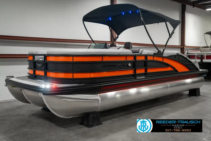 Slide: The Image of 2025 Bennington 23 RSB pontoon boat with orange accents and canopy in showroom. - 3