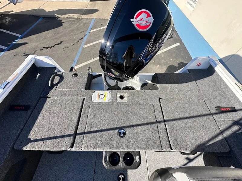 Slide: The Image of 2025 Lund 1775 Impact XS Sport boat interior with motor, gray carpet, and storage compartments. - 17