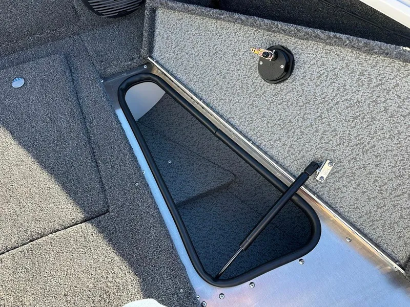 Slide: The Image of 2025 Lund 1775 Impact XS Sport boat storage compartment with open hatch and carpeted interior. - 26