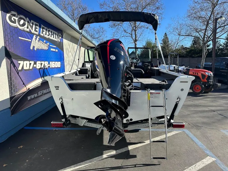 Slide: The Image of 2025 Lund 1775 Impact XS Sport boat with outboard motor and ladder, parked outdoors. - 7
