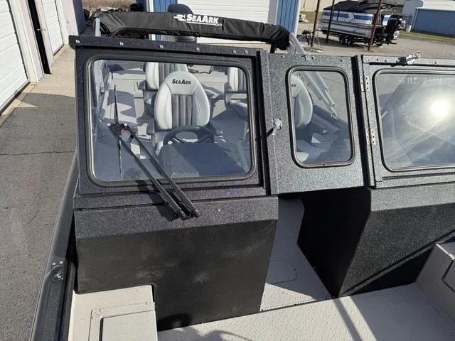 Slide: The Image of 2025 SeaArk Pro Cat 240 boat with windshield and seating, parked near storage units. - 10