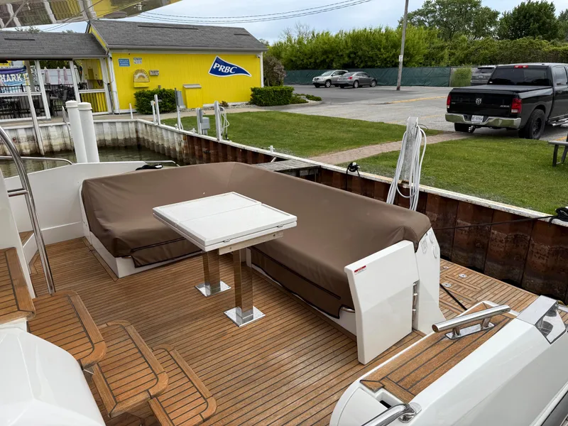 Slide: The Image of 2018 Galeon 560 Sky yacht deck with seating and table, docked near a yellow building. - 49