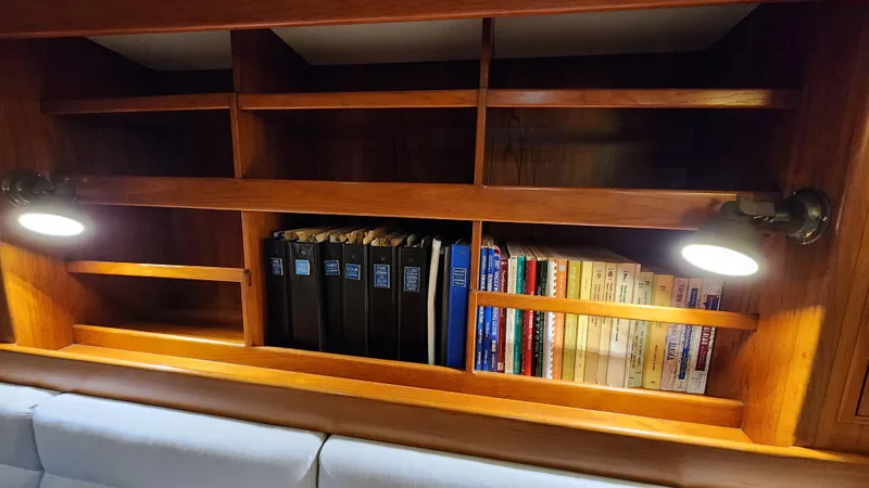 Slide: The Image of Wooden bookshelf with books and binders, illuminated by lights, inside a 1983 Nautor Swan 651 yacht. - 28