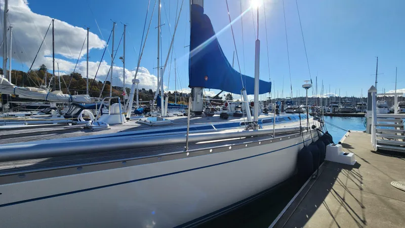 Slide: The Image of 1983 Nautor Swan 651 yacht docked in a sunny marina, featuring sleek design and blue sail cover. - 4