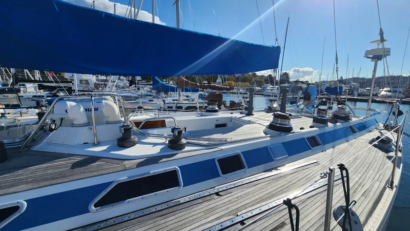 Slide: The Image of 1983 Nautor Swan 651 yacht docked in a sunny marina, showcasing sleek design and blue accents. - 5