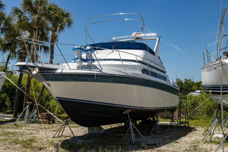 Slide: The Image of 1989 Carver 340 Santego boat on stands, surrounded by palm trees under a clear blue sky. - 5