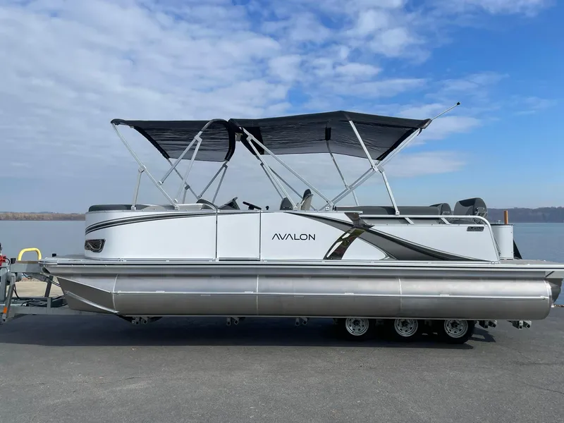 Slide: The Image of 2025 Avalon LSZ Quad Lounger Shift pontoon boat with canopy on a trailer by the water. - 1
