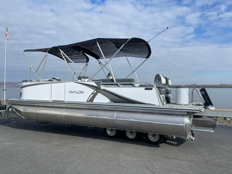 Slide: The Image of 2025 Avalon LSZ Quad Lounger Shift pontoon boat with canopy, parked by a lake. - 2