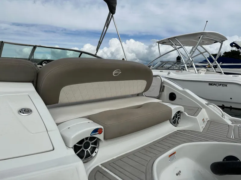 Slide: The Image of 2020 Crownline E235XS boat with beige seating and speakers, docked beside another boat. - 5