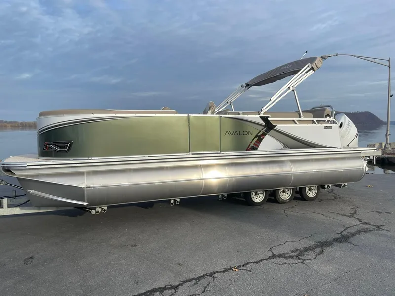 The Image of 2025 Avalon LSZ Cruise Rear Bench pontoon boat on trailer, parked by waterfront. - 1