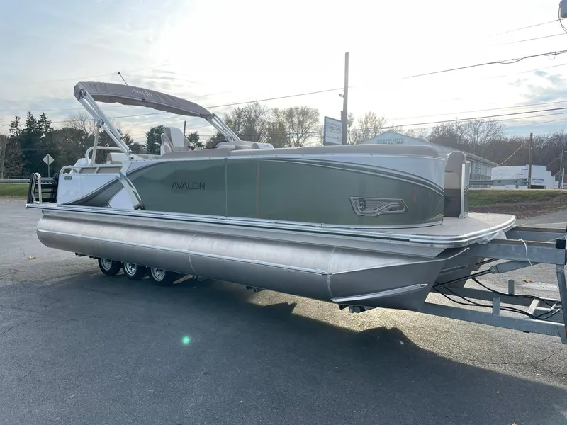 Slide: The Image of 2025 Avalon LSZ Cruise Rear Bench pontoon boat on trailer, parked outdoors. - 7