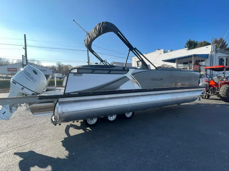 Slide: The Image of 2025 Avalon LSZ ELITE pontoon boat with Suzuki outboard motor, parked outdoors. - 7