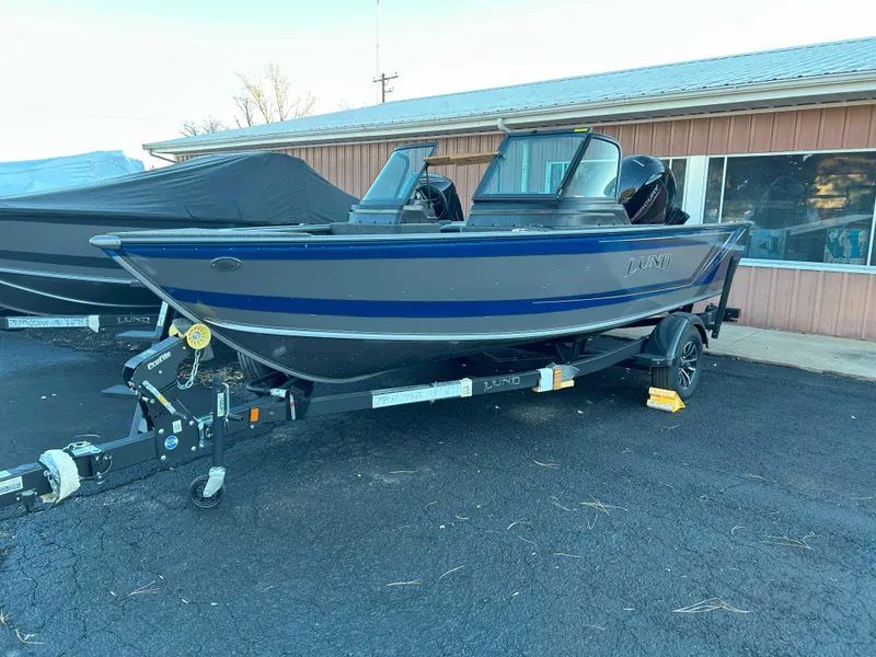 Slide: The Image of 2025 Lund 1875 Impact XS boat on trailer, parked outside a building. - 2