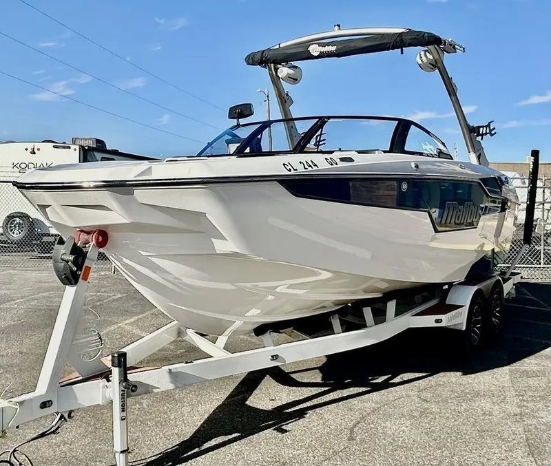 Slide: The Image of 2023 Malibu M220 boat on trailer, parked outdoors under clear sky. - 7