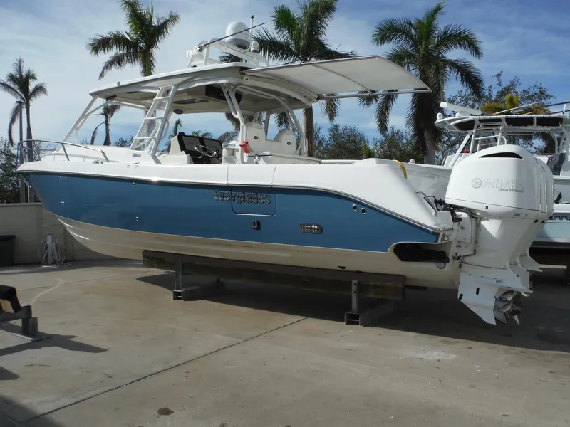 Slide: The Image of 2017 Everglades 360LXC boat with blue hull, docked on land, palm trees in background. - 10