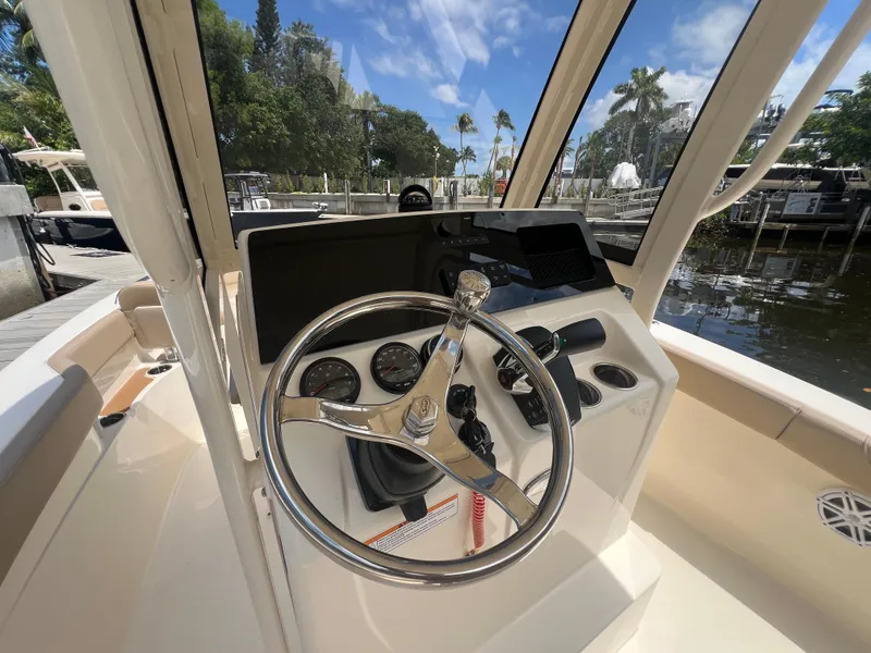 Slide: The Image of 2025 Scout 215 XSF boat dashboard with steering wheel and gauges, docked near lush greenery. - 7