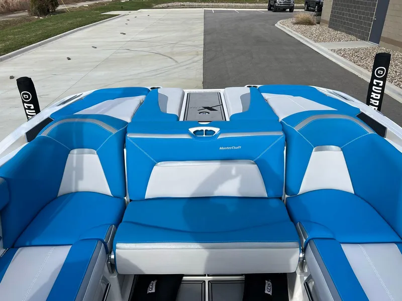 Slide: The Image of 2018 MasterCraft XStar boat with blue and white seating, parked on a paved area. - 11