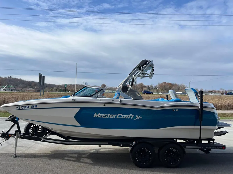 Slide: The Image of 2018 MasterCraft XStar boat on trailer, blue and white design, parked outdoors. - 4