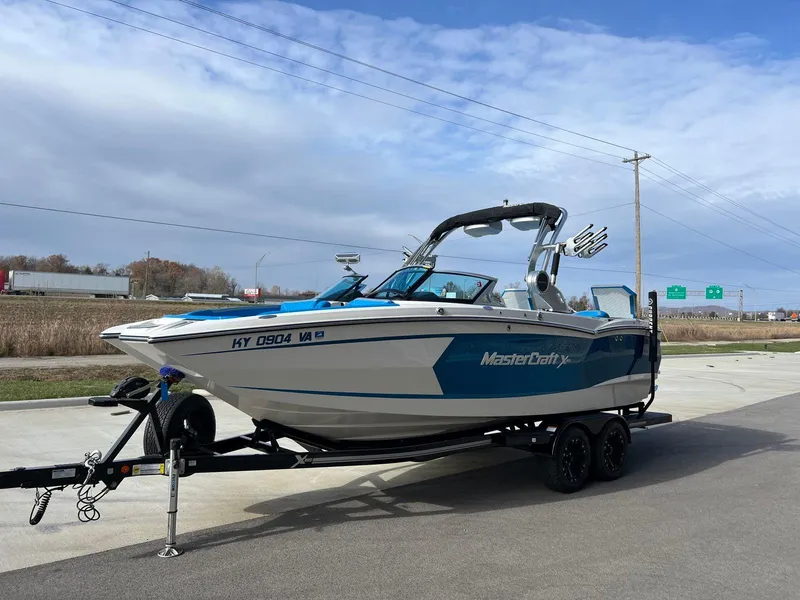 Slide: The Image of 2018 MasterCraft XStar boat on trailer, blue and white design, parked outdoors. - 6