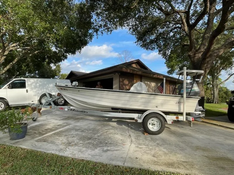 Slide: The Image of 1998 Hewes Bayfisher boat on trailer in driveway, surrounded by trees and a house. - 2