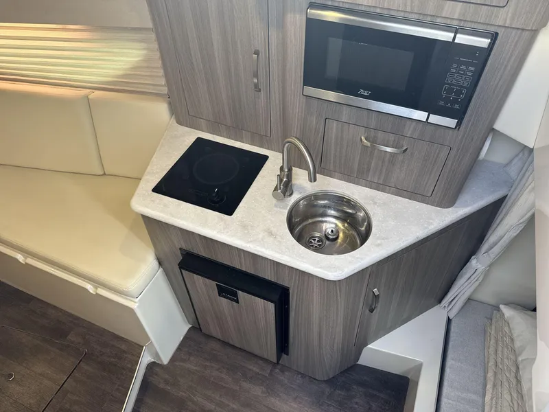 Slide: The Image of 2023 Regal 28EX boat interior kitchen with sink, stove, and microwave. - 17