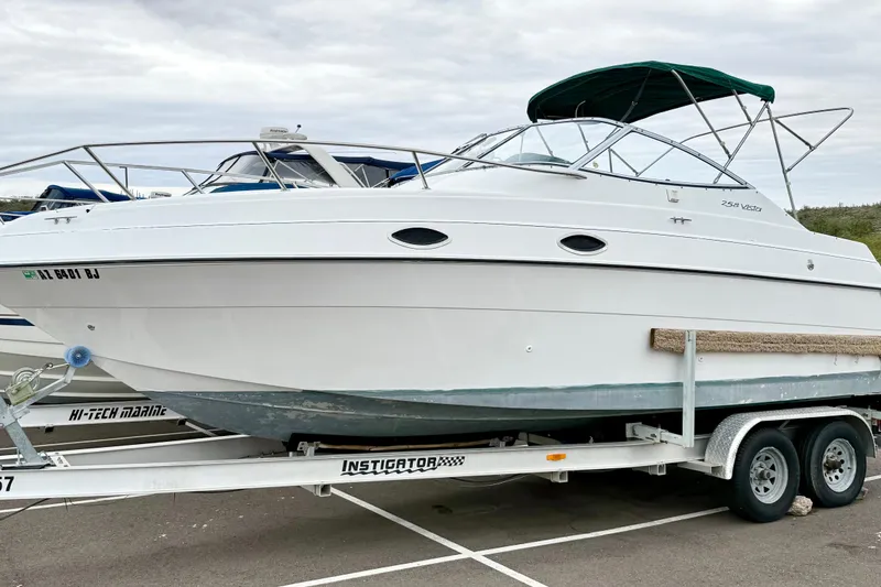 Slide: The Image of 1999 Four Winns 258 Vista boat on trailer, white hull, green canopy, parked outdoors. - 34