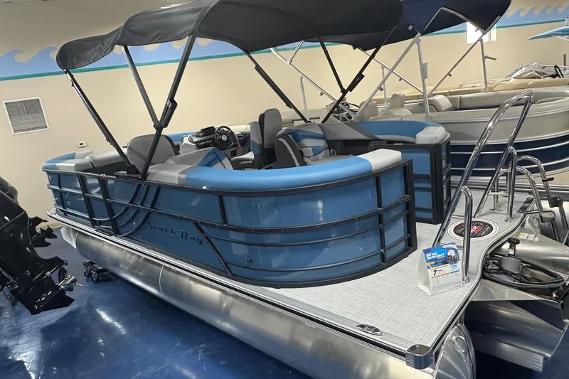 The Image of 2025 South Bay 200 pontoon boat with blue seating and canopy in showroom. - 0