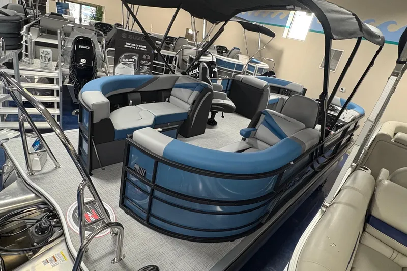 Slide: The Image of 2025 South Bay 200 pontoon boat with blue and gray seating in showroom. - 2