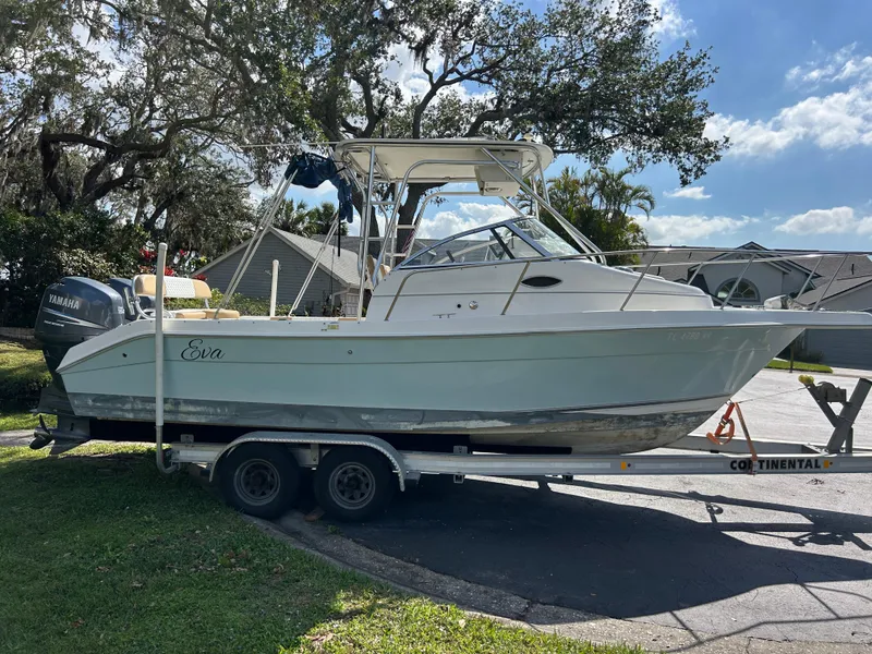 Slide: The Image of 2004 Cobia 250 Walk-Around boat on trailer, parked outdoors under a clear sky. - 11