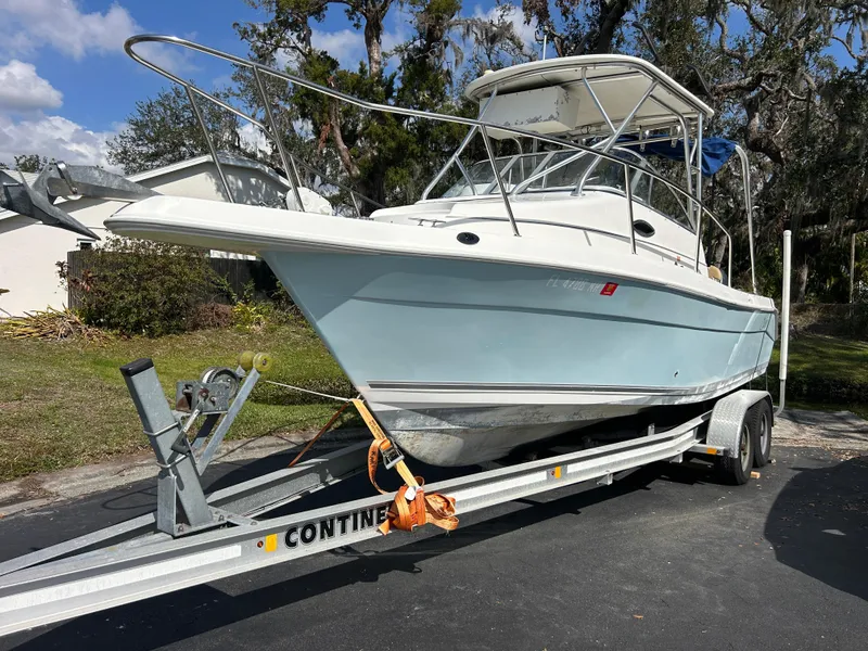 Slide: The Image of 2004 Cobia 250 Walk-Around boat on trailer, parked outdoors, under clear sky. - 6
