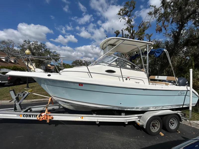 Slide: The Image of 2004 Cobia 250 Walk-Around boat on trailer, parked outdoors under a blue sky. - 7