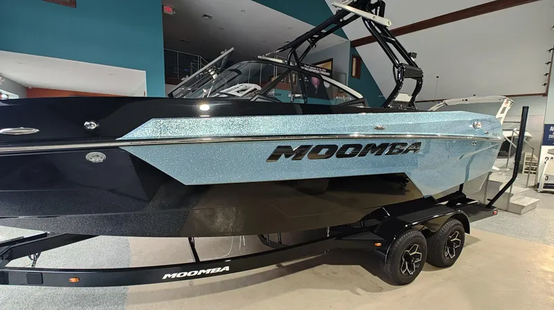 Slide: The Image of 2025 Moomba Max boat in showroom, sleek design with metallic blue finish. - 1